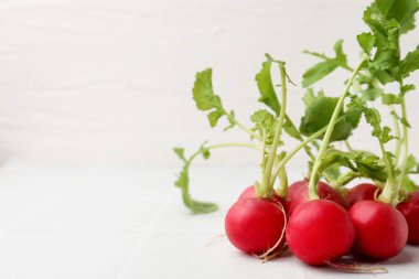 Fresh radishes with green leaves on white tiled table, closeup. Space for text