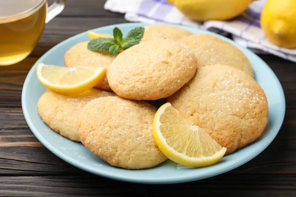 Lezzetli limonlu kurabiyeler ve siyah ahşap masada meyve dilimleri, yakın plan.