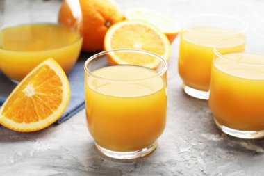 Taze portakal suyu ve meyveler gri masada, yakın plan.