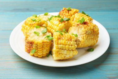 Mavi ahşap masada yeşil soğanlı ızgara mısır koçanı parçaları, yakın plan.