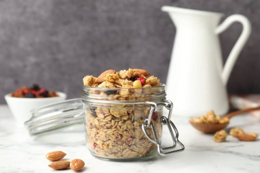 Lezzetli granola, cam kavanozda kurutulmuş meyveler, beyaz mermer masada, yakın plan.
