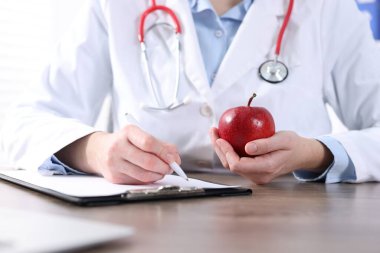 Ahşap masada çalışan olgun elmalı bir doktor, yakın plan.