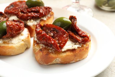 Krem peynirli lezzetli bruschettalar, güneşte kurutulmuş domatesler ve yeşil zeytinler masada, yakın plan.