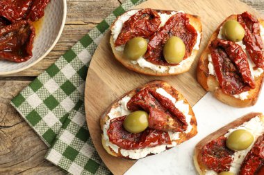 Krem peynirli lezzetli bruschettalar, güneşte kurutulmuş domatesler ve ahşap masada yeşil zeytinler.