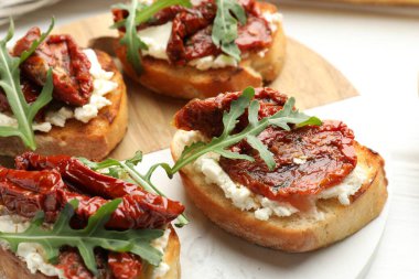 Krem peynirli lezzetli bruschettalar, güneşte kurutulmuş domatesler ve masanda roka, yakın plan.