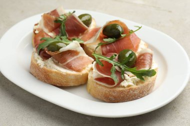 Krem peynirli lezzetli bruschettalar, prosciutto, yeşil zeytin ve roka gri dokulu masa, yakın plan.