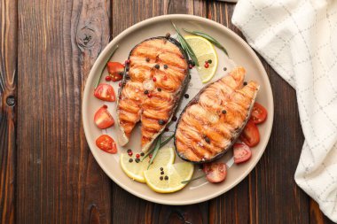 Lezzetli ızgara somon bifteği, limon, biberiye ve ahşap masada domatesle servis edilir.