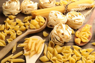 Farklı türde çiğ makarna ve çiviler, ahşap masa, yakın plan.