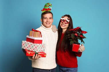 Noel aksesuarları, saksısı ve açık mavi arka planda hediyeleri olan mutlu çift.