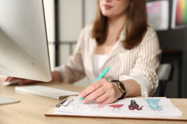 Ofisteki ahşap masadaki bilgisayarda çalışırken tasarımcı giysilerin taslağını çiziyor.