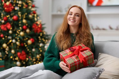 Kanepede Noel hediyesi olan süveterli bir kadın rahat bir odada bulanık ışıklara karşı. Metin için boşluk