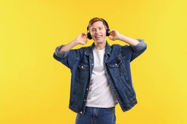 Kulaklıklı adam sarı arka planda müzik dinliyor.