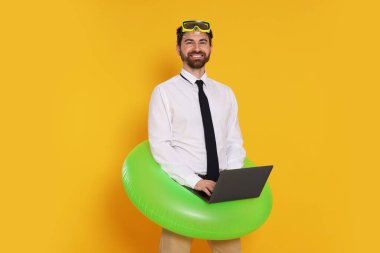 Dalış maskesi, dizüstü bilgisayarı ve turuncu arka planda şişme yüzüğü olan bir iş adamı.