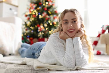 Yerde süveter giymiş gülümseyen bir kadın. Odadaki bulanık ışıklara karşı. Noel için süslenmiş.