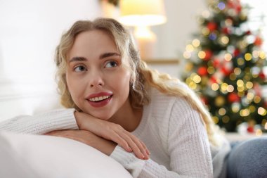 Evdeki bulanık ışıklara karşı kanepede süveter giyen gülümseyen kadın. Mutlu Noeller ve mutlu yıllar.