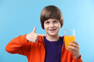 Açık mavi arka planda taze portakal suyu bardağını gösteren çocuk.