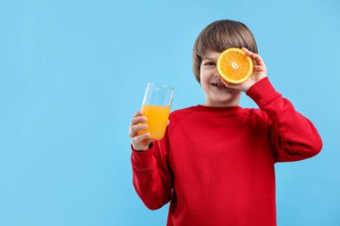 Açık mavi arka planda bir bardak taze portakal suyu ve meyveli çocuk. Metin için boşluk