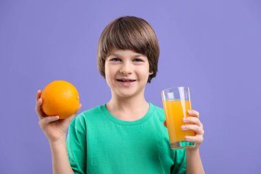 Menekşe arka planında bir bardak taze portakal suyu ve meyvesi olan çocuk.