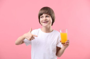 Çocuk pembe arka planda taze portakal suyu bardağını işaret ediyor.