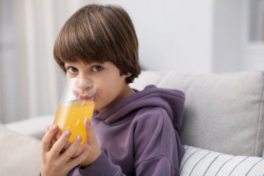 Çocuk evdeki kanepede taze portakal suyu içiyor. Metin için boşluk