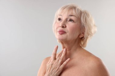 Üst düzey kadın açık gri arka planda boynuna dokunuyor. Metin için boşluk