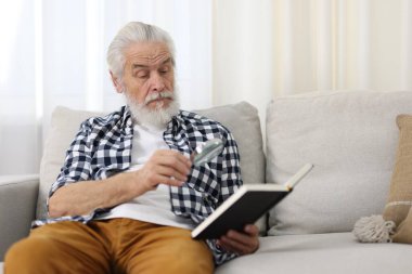 Üst düzey bir adam kanepede kitap okurken büyüteç kullanıyor.