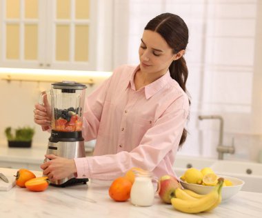 Mutfaktaki beyaz mermer masada blender ile nefis smoothie yapan bir kadın.