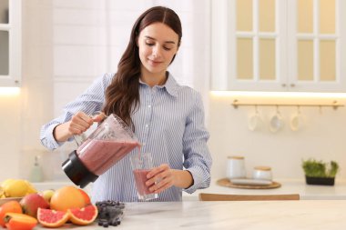 Mutfaktaki beyaz mermer masada, blenderdan cama leziz meyve püresi döken bir kadın. Metin için boşluk