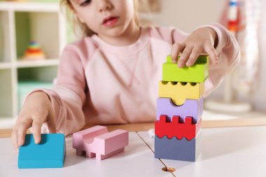 Oyun odasındaki beyaz masada oyuncaklarla oynayan mutlu küçük kız, seçici odaklanma