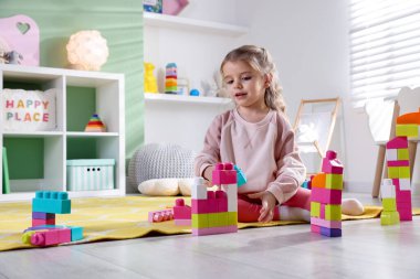Küçük kız oyun odasında yerde oyuncaklarla oynuyor.