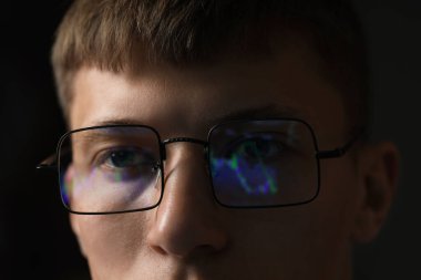 Siyah arka planda yansıması olan gözlüklü genç adam, yakın plan.