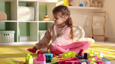 Küçük kız oyun odasında yerde oyuncaklarla oynuyor.