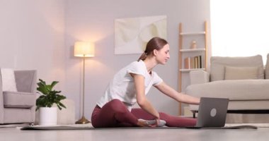 Hamile bir kadın evde dizüstü bilgisayarla yoga dersi alıyor.