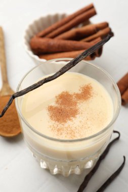 Bardakta lezzetli protein karışımı, beyaz masada tarçın ve vanilya kapsülleri, yakın plan.