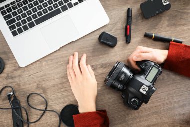Ahşap masada dizüstü bilgisayarı, kamerası ve diğer aletleri olan profesyonel bir fotoğrafçı.
