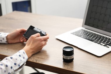 Ahşap masada dizüstü bilgisayarı, kamerası ve lensi olan profesyonel fotoğrafçı, yakın plan.