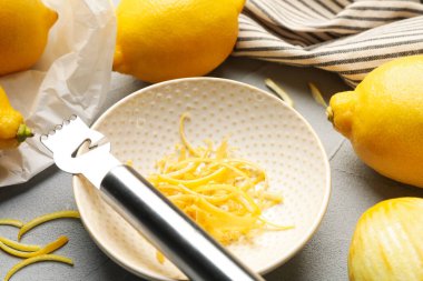 Gri masada zevkli ve zester aletli taze limonlar, yakın plan.