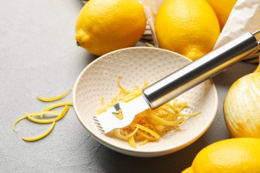 Gri masada zevkli ve zester aletli taze limonlar, yakın plan.