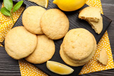 Lezzetli limonlu kurabiyeler ve koyu ahşap masada meyve dilimleri, düz uzanmış.