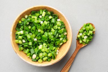 Yeşil soğanı kasede ve kaşıkla kes gri masada, düz uzan