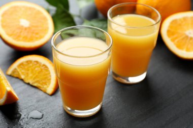 Taze portakal suyu ve siyah masada meyveler, yakın plan.