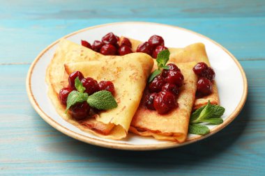 Açık mavi ahşap masada kiraz reçeli ile servis edilen leziz krepler, yakın plan.