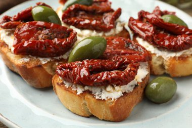 Krem peynirli lezzetli bruschettalar, güneşte kurutulmuş domatesler ve yeşil zeytinler masada, yakın plan.