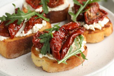 Krem peynirli lezzetli bruschettalar, güneşte kurutulmuş domatesler ve masanda roka, yakın plan.