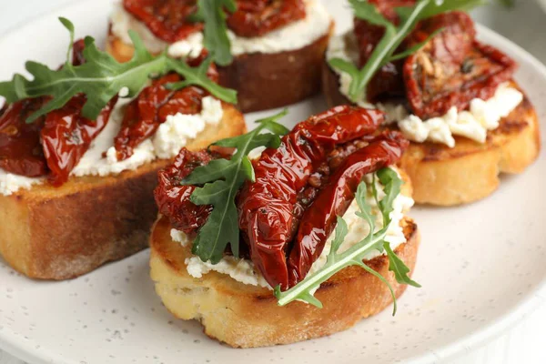 Krem peynirli lezzetli bruschettalar, güneşte kurutulmuş domatesler ve masanda roka, yakın plan.