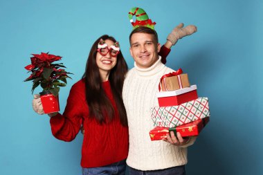 Noel aksesuarları, saksısı ve açık mavi arka planda hediyeleri olan mutlu çift.