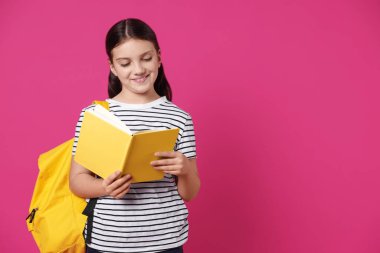 Pembe arka planda kitabı ve sırt çantası olan tatlı bir kız. Mesaj için yer var.