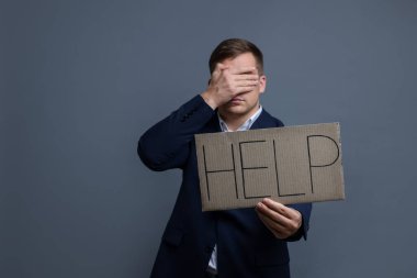 Man holding cardboard sign with word Help on grey background