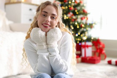 Evdeki bulanık ışıklara karşı eldivenli ve kazaklı gülümseyen kadın portresi. Mutlu Noeller ve mutlu yıllar.