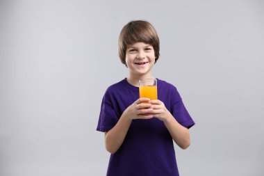 Açık gri arka planda bir bardak taze portakal suyu olan çocuk. Metin için boşluk